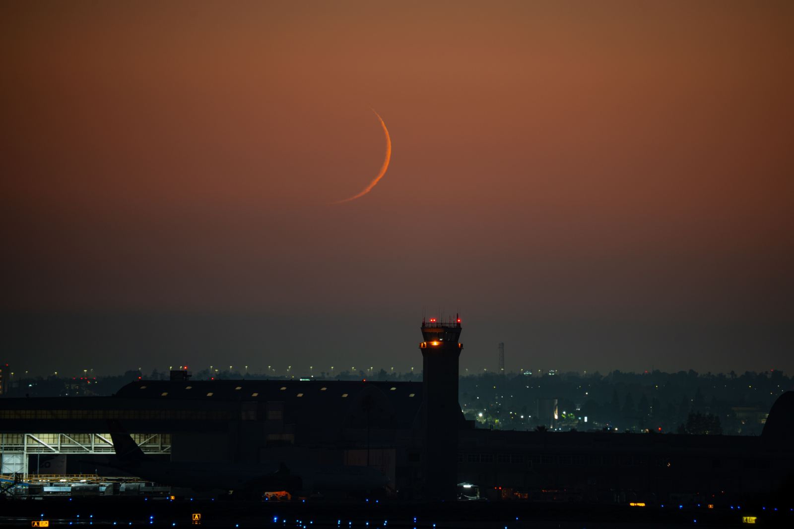 Airport control tower silhouetted at dusk under a crescent moon
