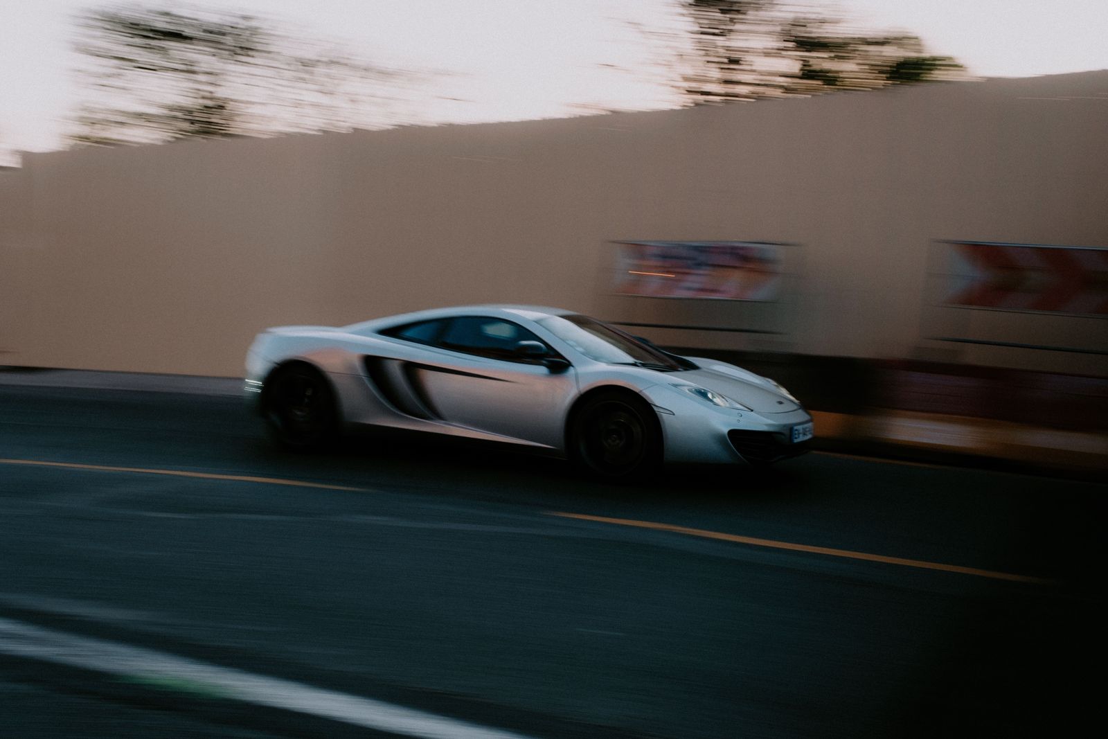A silver sports car moving along a city street at dusk