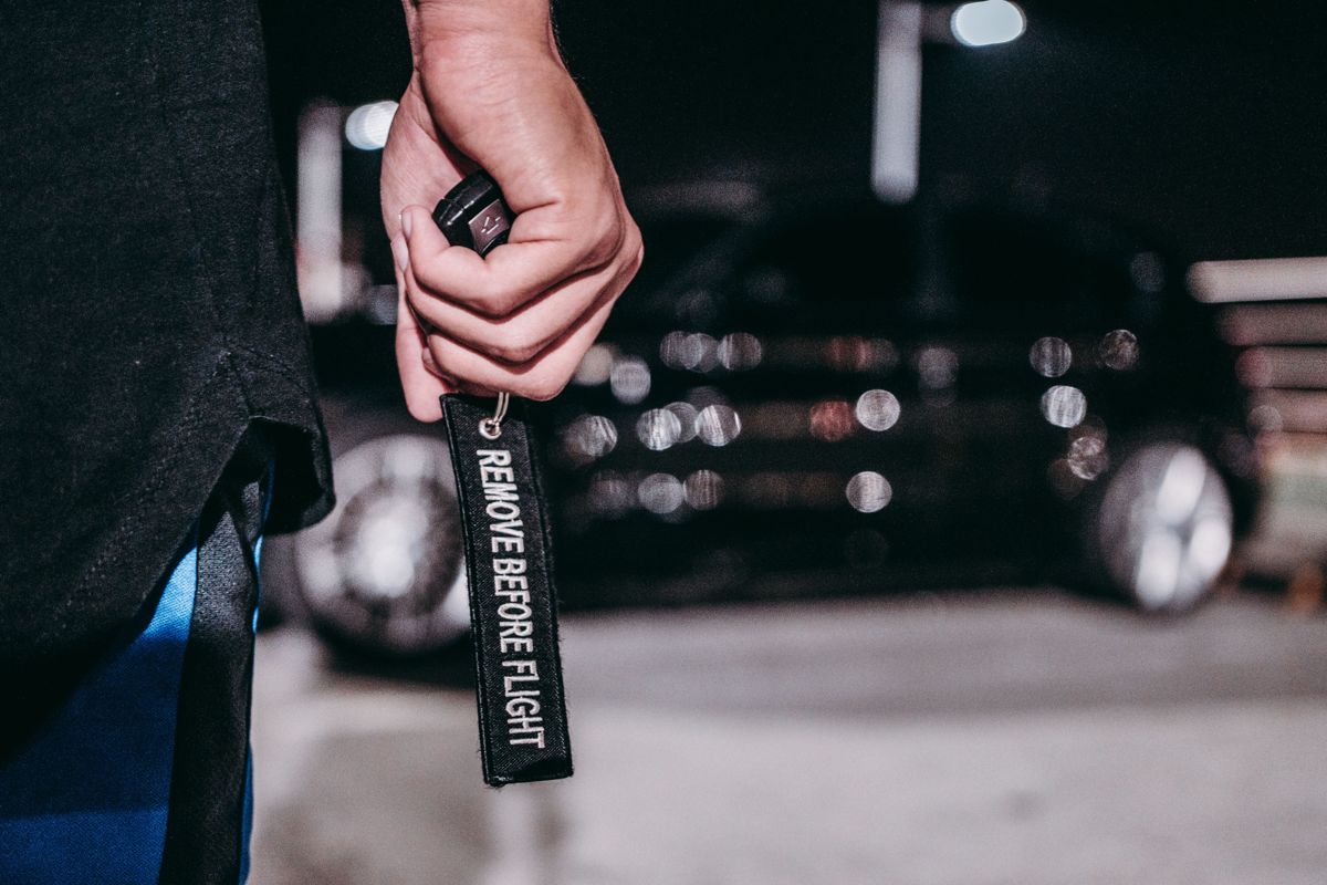 A hand holding a car key fob at night with cars blurred behind