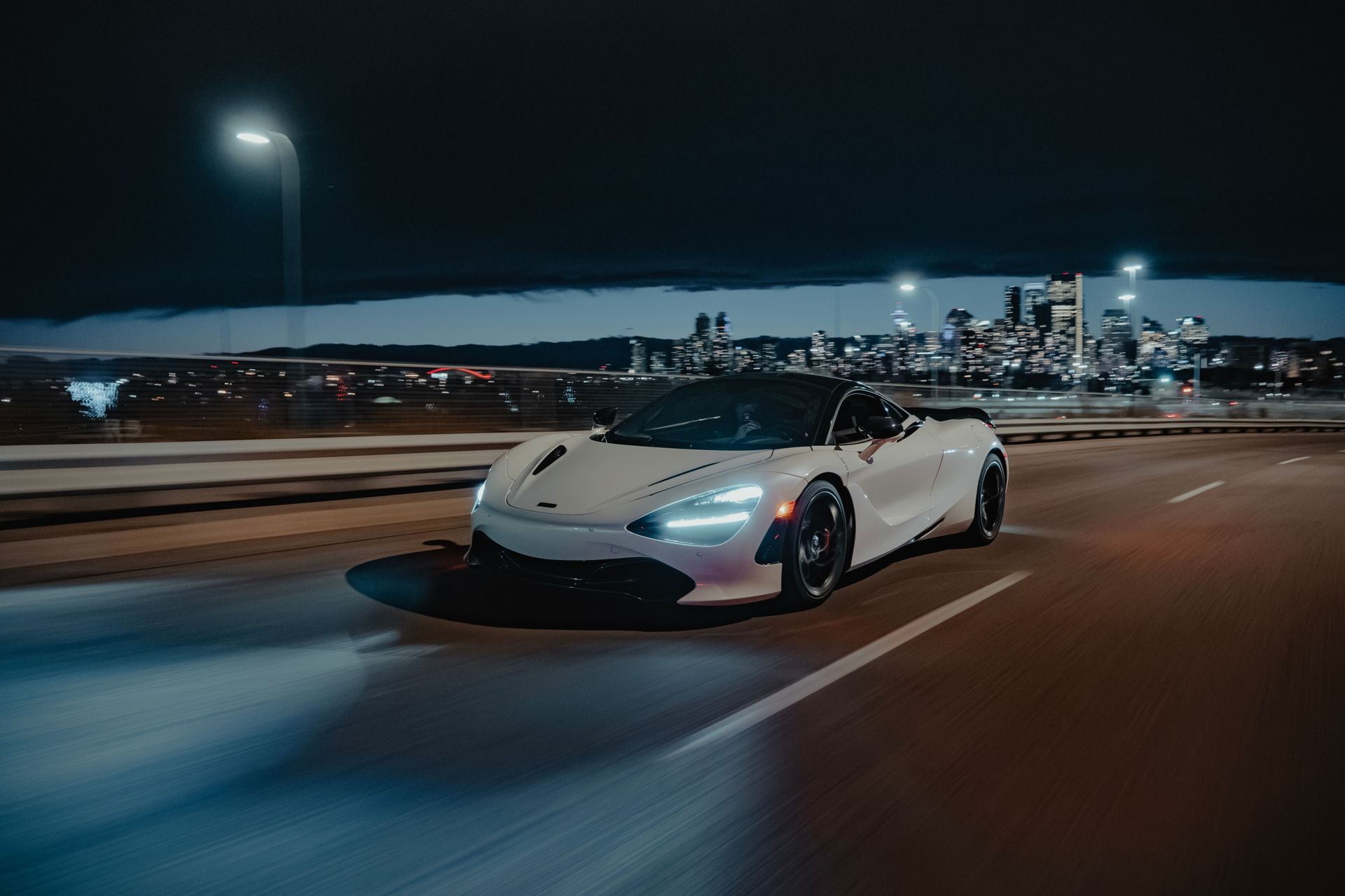 White McLaren supercar driving at night with a city skyline behind